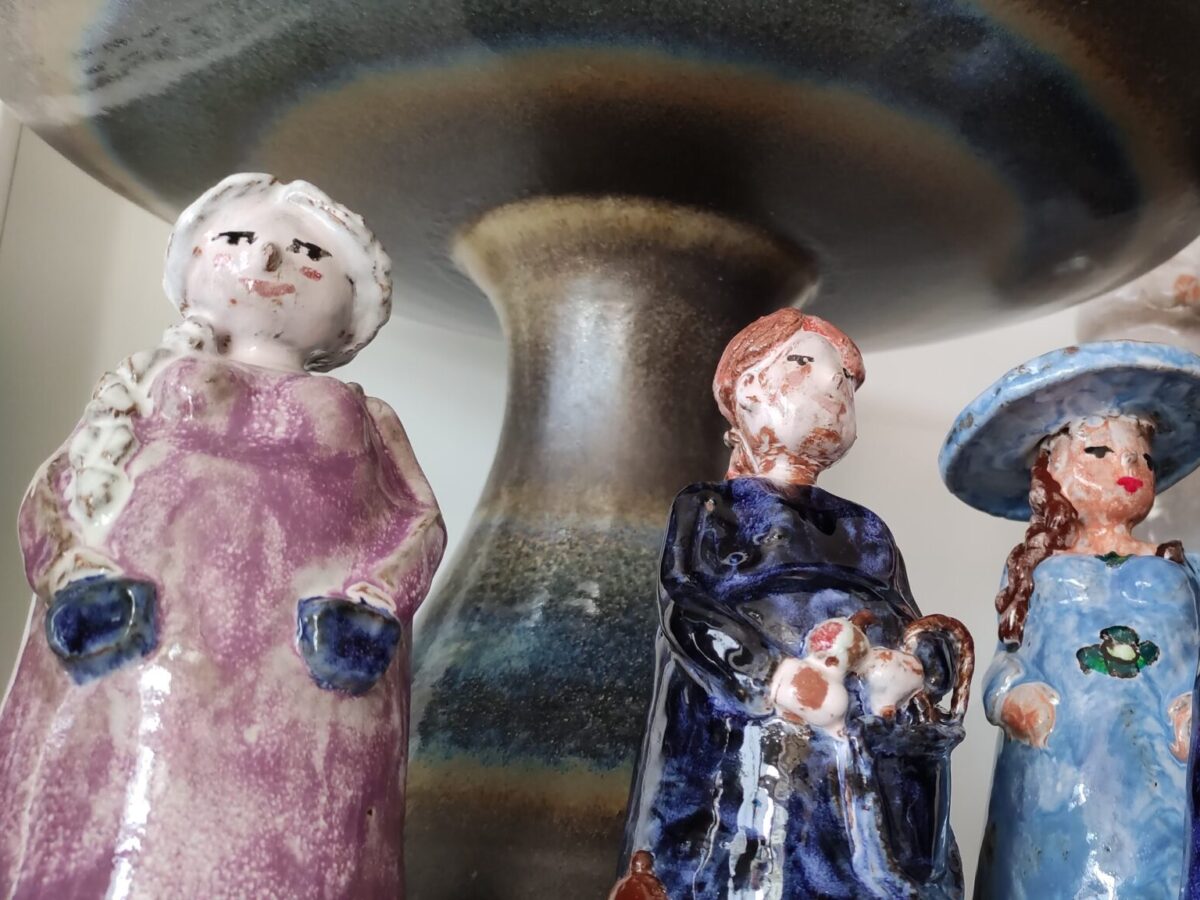 Mehrere Keramikfiguren, die Menschen darstellen und eine Vase stehen in einem Ladenregal.